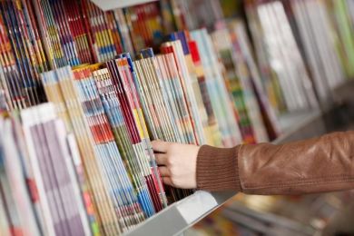 revistas numa estante numa tabacaria com uma pessoa a escolher uma revista
